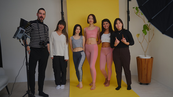 Behind the scenes footage of a photo shooting. Photographers videographers female models director and make-up artist are working together in a studio.