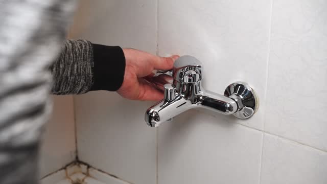 Male Plumber fixing repairing leaky shower Bathtub water tap faucet by wrench tool, unrecognizable man working at home