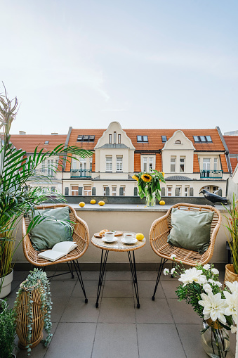 Vertical shot of open space on summer terrace, balcony on roof of hotel with view of cityscape. Wicker armchairs with cushions, round coffee table with breakfast against old historical city center