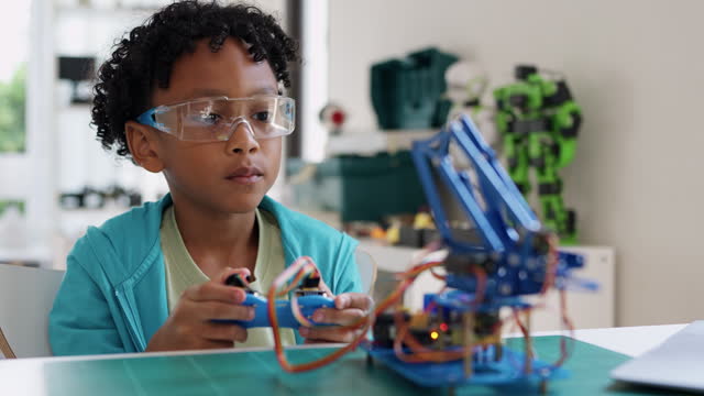 A young black child is deeply engaged in writing coding to control a mechanical arm in his living room. Engaging in online e-learning with expert teachers, the child demonstrates curiosity, creativity, and a passion for STEM topics.