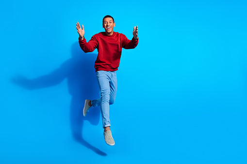 Full length photo of friendly cheerful man jump raise opend arms welcome you empty space isolated on blue color background.