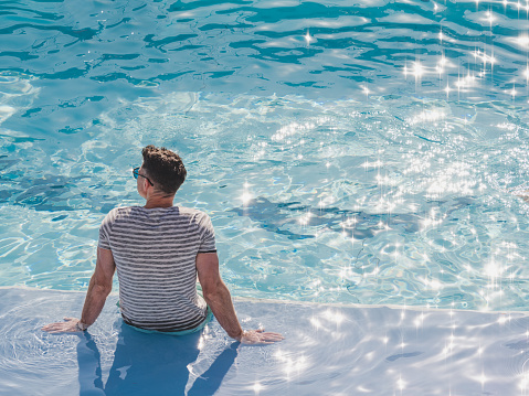 Handsome man sitting near the swimming pool of a cruise ship. Sunny morning, clear day. View from above. Closeup, outdoor. Vacation and travel concept
