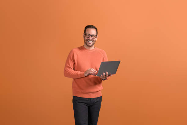 istock Portrait of happy confident businessman checking e-mails over wireless computer on orange background 2147585108