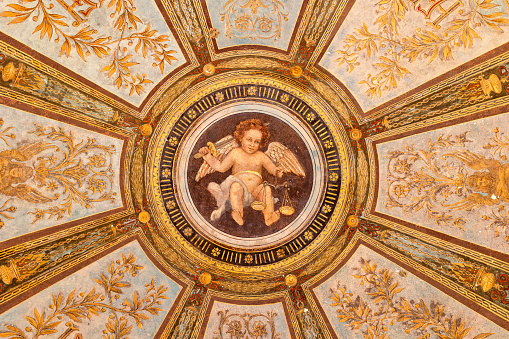 Painted ceiling decoration depicting a baby angel inside ornate medallion. Close-up of old arcades at Vienna Central Cemetery with graves from 1880s