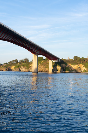 A bridge spans a body of water, with a view of the shoreline in the background. The water is calm and clear, reflecting the sky above. The bridge is a vital link between two areas