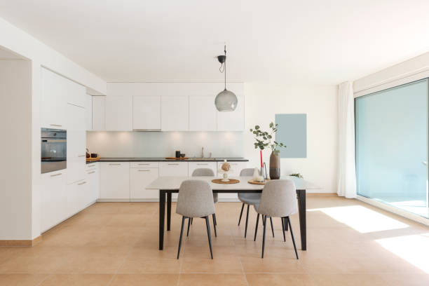Large modern white kitchen with a marble table and four chairs in front. This is the interior of a modern flat.