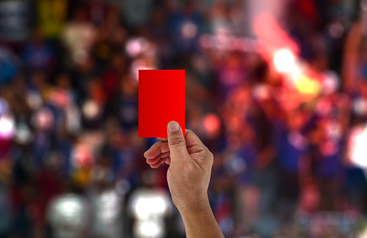 The referee raises his hand and shows a red card in a football match.