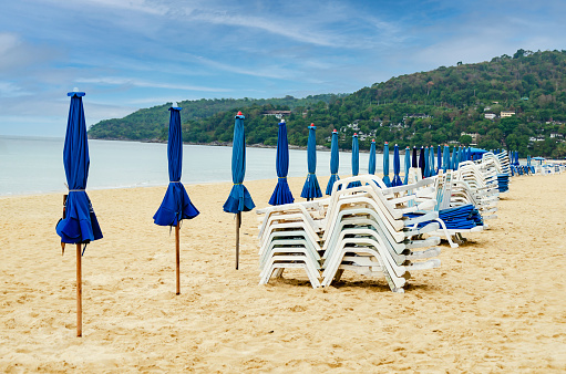 Folded beach umbrellas and sun loungers on an empty beach on a cloudy day