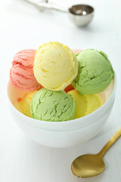 Bowl with ice cream scoops on white wooden table
