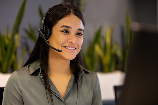 Latin American customer service representative working at a call center using a headset and smiling