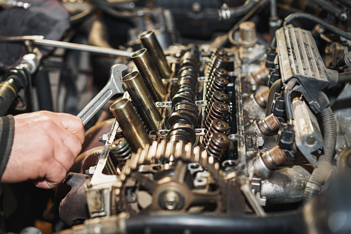 The mechanic is repairing a car engine. He is holding a wrench in his hand. Cylinder head. Valve. Sixteen valves. Valve springs. Engine block. Car repairing. Auto service.