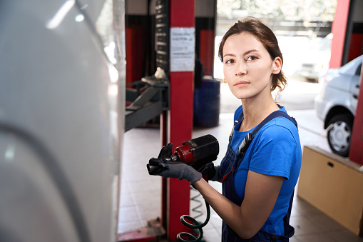 Woman auto mechanic works with a car on a car lift, the specialist uses a pneumatic wrench