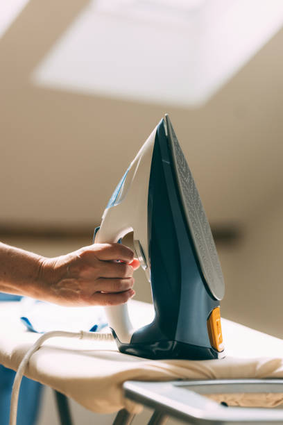 A focused mature woman efficiently ironing and folding laundry in the comfort of her sunlit home.
