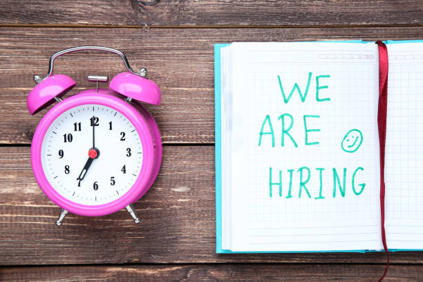 istock Text We Are Hiring in notepad with alarm clock on wooden table 2147597667