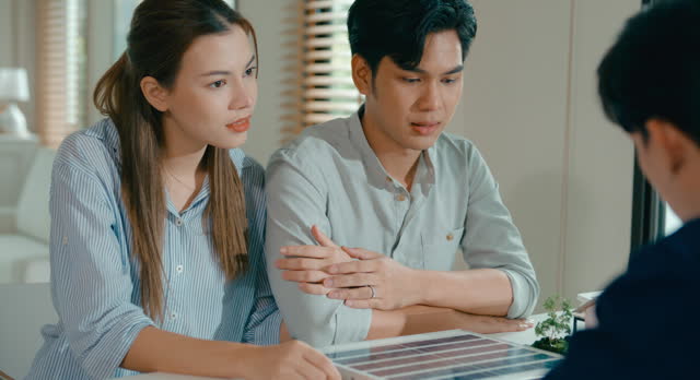 Young Asian couple in detailed consultation with real estate agent, who is highlighting advantages of home with solar panels. Consulting on Eco-Friendly Home Ownership with Real Estate Agent.