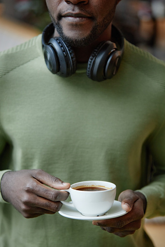Vertical closeup of young African American man holding simple coffee cup against green crewneck shirt