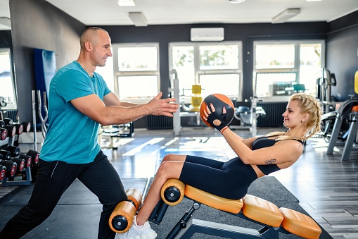 Personal trainer helping women working sit-ups with a medicine ball