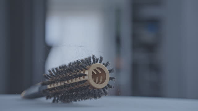 Black hair tangled in hair brush spins on grey surface
