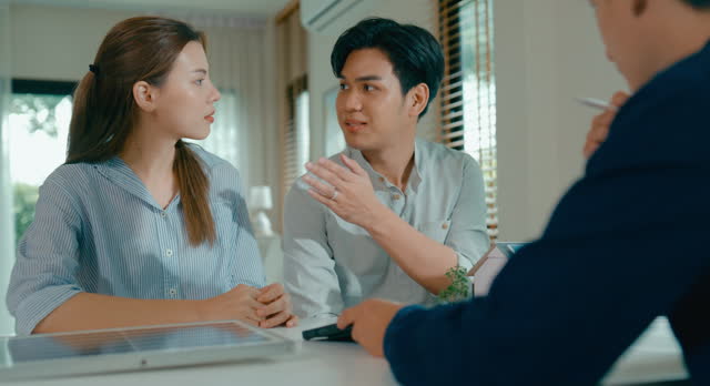 Closeup of young Asian couple discussion real estate agent about financial and environmental benefits of investing in home with solar technology. Eco-Friendly Home with Real Estate Agent.