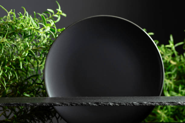 Black stone podium, black ceramic plate and branches of rosemary.