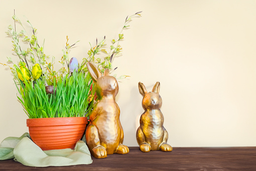 blooming potted spring flowers standing on a wooden shelf, front view of decorative rabbit figurines, copy space for a text. Easter Celebration Concept. High quality photo