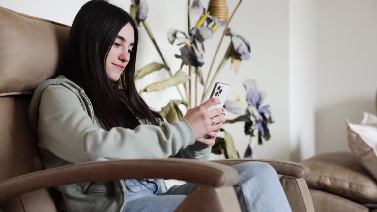 A beautiful girl enjoys a moment of relaxation on a cozy sofa, engrossed in their smartphone.