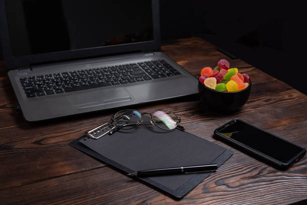 Desk in the office. Laptop and sweets on the table. Glasses and notepad on the surface. View from above at an angle