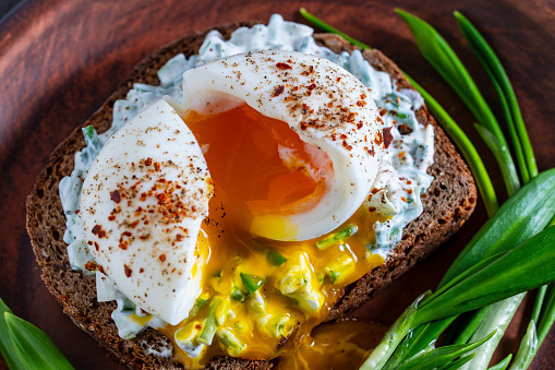 Delicious sandwich with bread, salad of green wild garlic, soft-boiled egg and sour cream on plate, close up