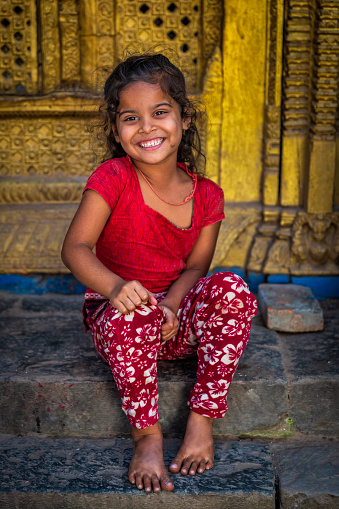 Portrait of little Nepali girl sitting in an ancient temple in Bhaktapur. Bhaktapur is an ancient town in the Kathmandu Valley and is listed as a World Heritage Site by UNESCO for its rich culture, temples, and wood, metal and stone artwork.