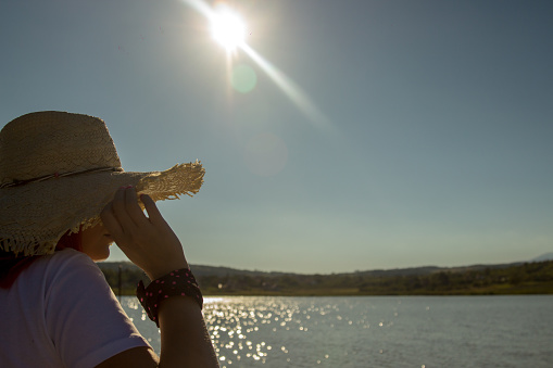 Woman is wearing straw hat looking on the beautiful lake