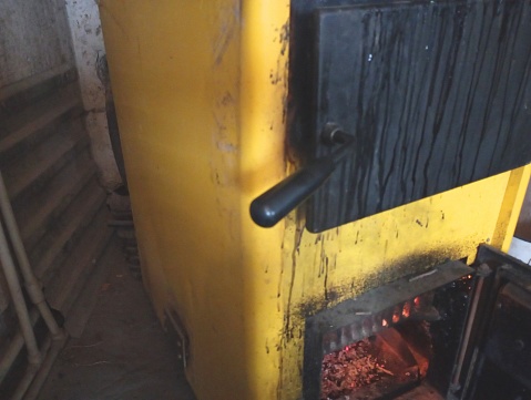 A yellow wood-burning boiler in which fire is burning for heating the house. House heating system with a solid fuel boiler.
