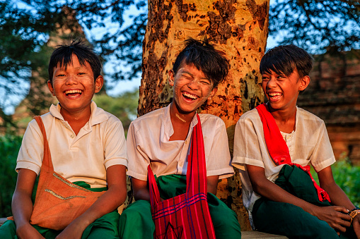 Young Burmese schoolboys with thanaka sitting under the tree, Nyaung-U, Myanmar (Burma)