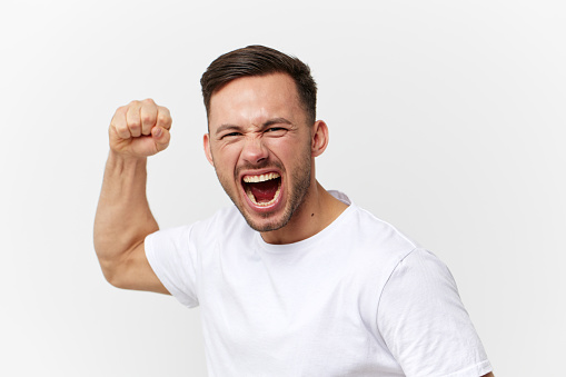 Aggressive angry crazy young tanned handsome man in basic t-shirt swings fist posing isolated on over white studio background. Copy space Banner Mockup. People emotions. Abusive relationships concept