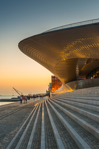 The iconic ceramic tiles of the MAAT Museum of Architecture, Art and Technology spotlit at dusk overlooking the blue waterfront of the Tagus in the heart of Lisbon, Portugal’s vibrant capital city.