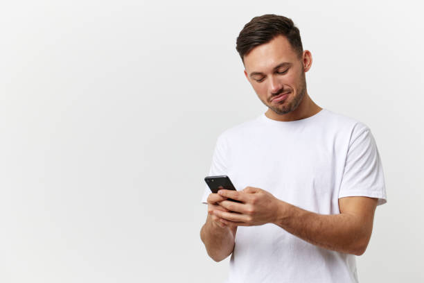 istock Happy passionate tanned handsome man in basic t-shirt doing online shopping with phone posing isolated on over white studio background. Copy space Banner Mockup. Mobile gaming RPG concept 2147609266
