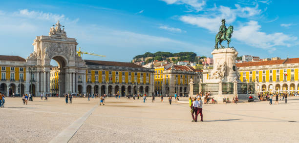 Tourists strolling through the warm sunshine in the Praca do Comercio, the landmark square overlooked by the historic Rua Augusta Arch in the heart of Lisbon, Portugal’s vibrant capital city.
