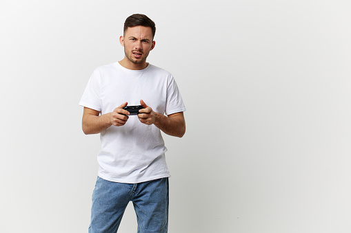 Confused irritated tanned handsome man in basic t-shirt failed game session with joystick gamepad posing isolated on over white studio background. Copy space Banner Mockup. Gamer RPG concept