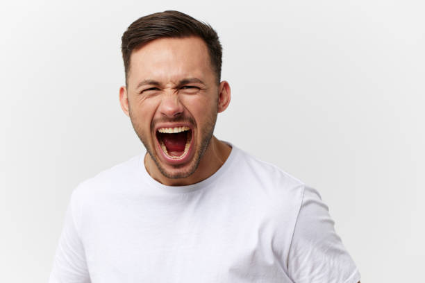 istock Aggressive evil tanned handsome man in basic t-shirt scream at camera posing isolated on over white studio background. Copy space Banner Mockup. People emotions. Domestic violence concept 2147610331