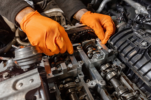 Experience the precision of a skilled mechanic's hands, clad in orange gloves, as they meticulously work under the hood to repair an open car engine in an auto service center, ensuring top-notch maintenance