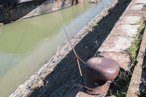 Old metal dock mooring pole with steel rope for securing river bulk barge ship closeup