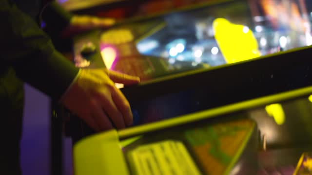 Focused hands maneuver pinball controls, camera's shaky movements amplify tension. Quick reflexes on vibrant machine, visuals quiver with player's intensity. Video highlights nerve-wracking gameplay