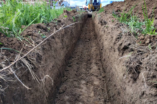Construction excavator digging a shallow groove for electrical wiring or cable.