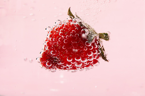 Strawberry in water against pink background, close up