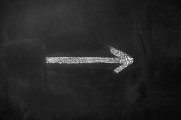 istock White arrow hand painted with chalk on a black blackboard indicating the direction 2147617341