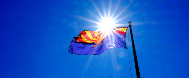 Arizona state flag flying in breeze on flagpole with sunshine sunstar in blue sky