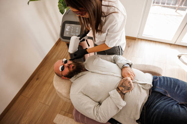 High angle view of young man having laser epilation of cheekbones in beauty salon