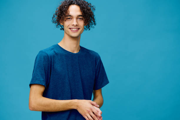 istock Smiling joyful cute curly tanned Caucasian guy in basic t-shirt posing isolated on over blue background. Lifestyle and Emotions concept. Good offer with copy space for ad 2147620440