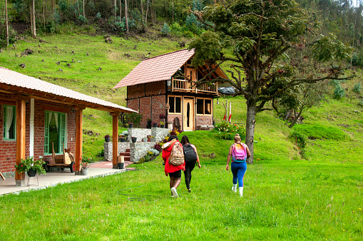 Friends walk towards a wooden cabin nestled in lush greenery, a tranquil escape into natures embrace.