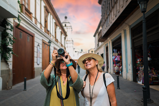 Two female tourists, one of them taking a photograph on a street in the historic city of Lima.