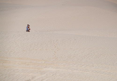 Side view of a woman  sitting and  photographing  morning at White dunes, called Sugar dunes at Al Khaluf, Oman. It is south part of Wahiba desert, near Arabian sea.